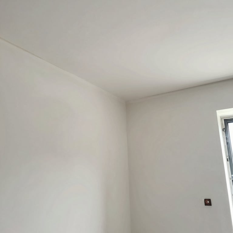 Interior finishing work showing perfectly plastered walls and smooth ceiling joints in a bright room.