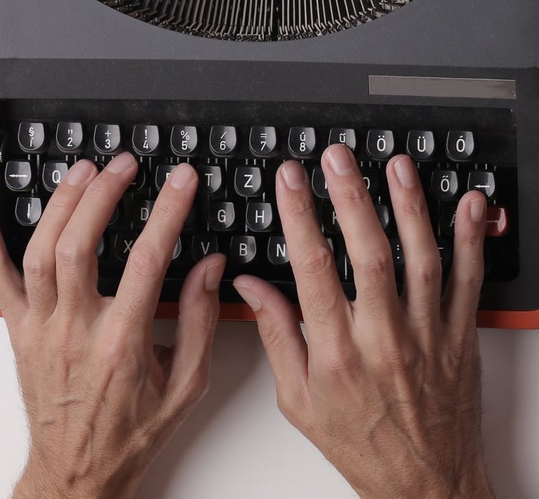 Hands typing on an orange and black typewriter with a blank sheet of paper.