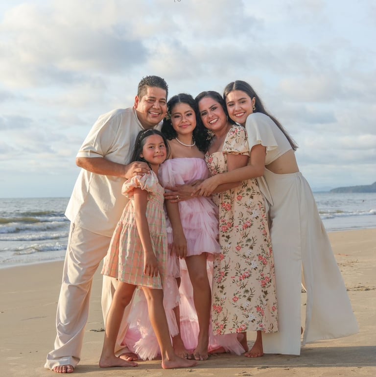 una familia de mamá, 3 hijas y papá sonriendo a la cámara en la playa