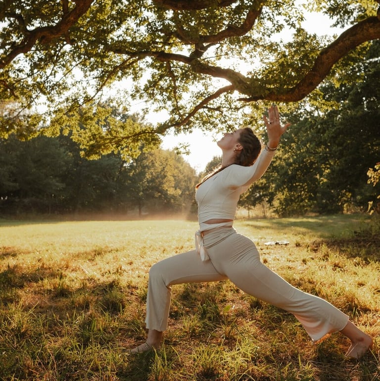 Eine Frau praktiziert Yoga im Krieger-1-Stand unter einem großen Baum in einer sonnigen Waldlichtung