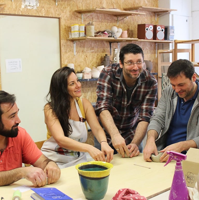 a group of people sitting around a table making pottery