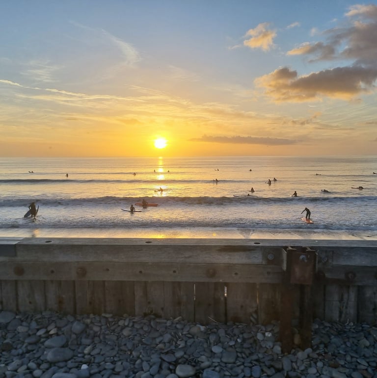 An amazing orange sun setting into the sea while. abusy after school club surf lesson goes on.