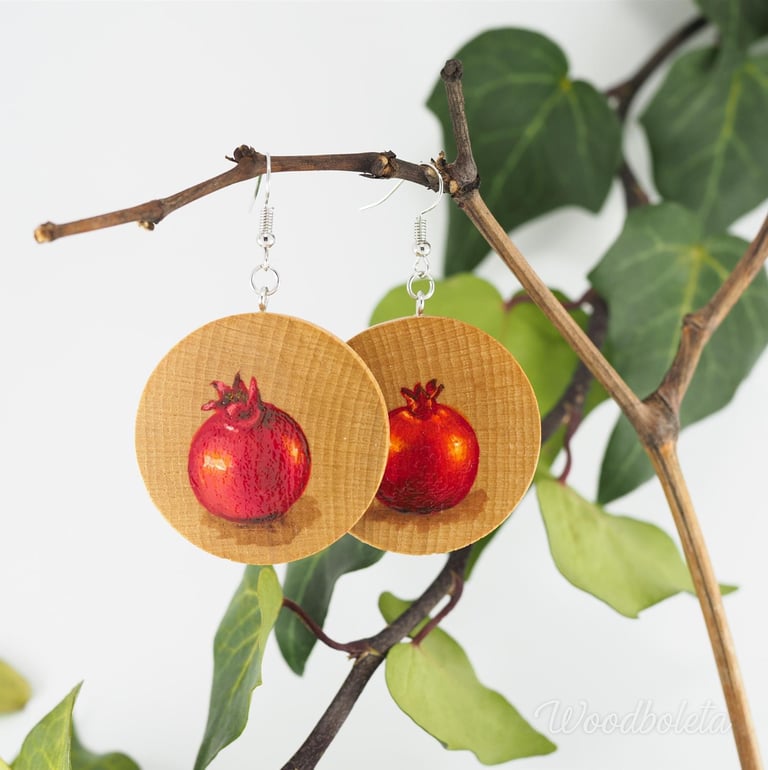 wooden earrings hand painted with pomegranates motif, hanging on branch