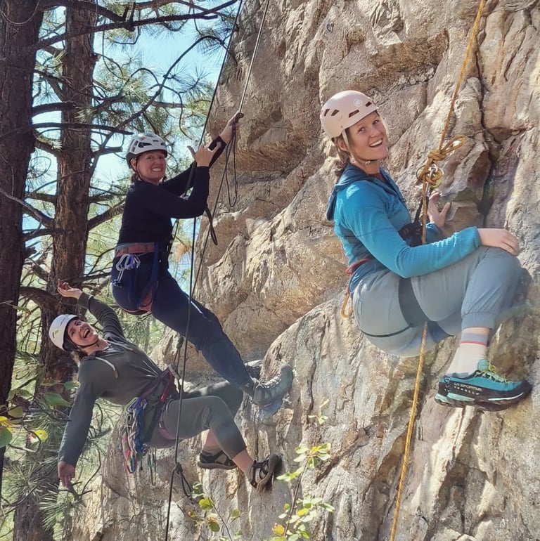 A group of three people smiling and hanging off ropes on an outdoor rock climb