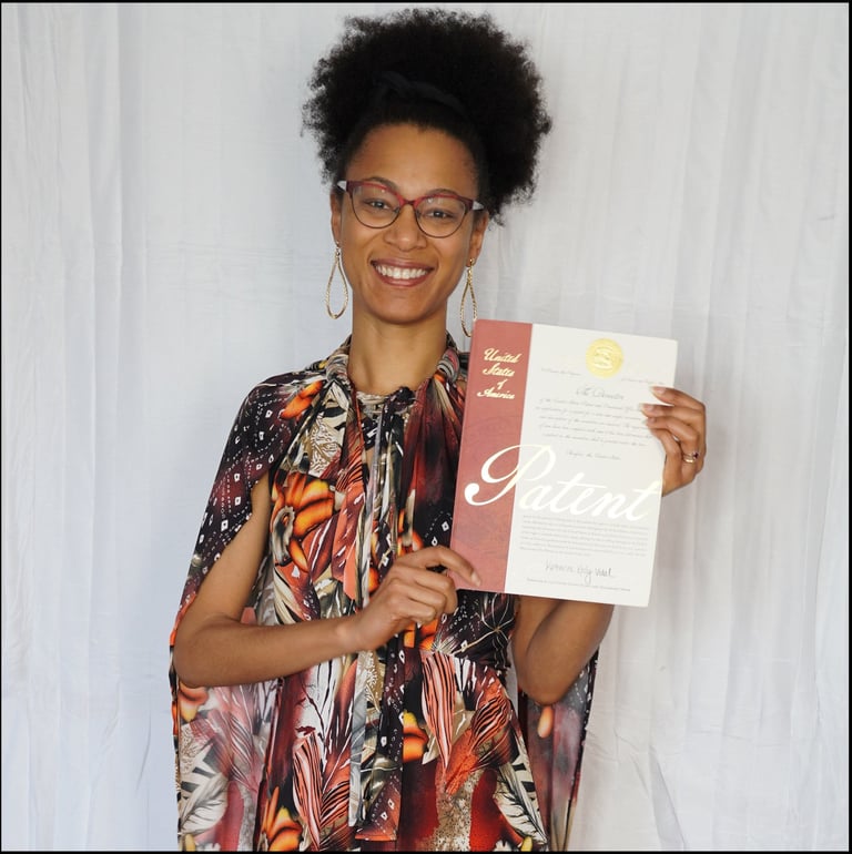 Photography of Ryan wearing a dress, smiling and holding her issued U.S. Patent document.
