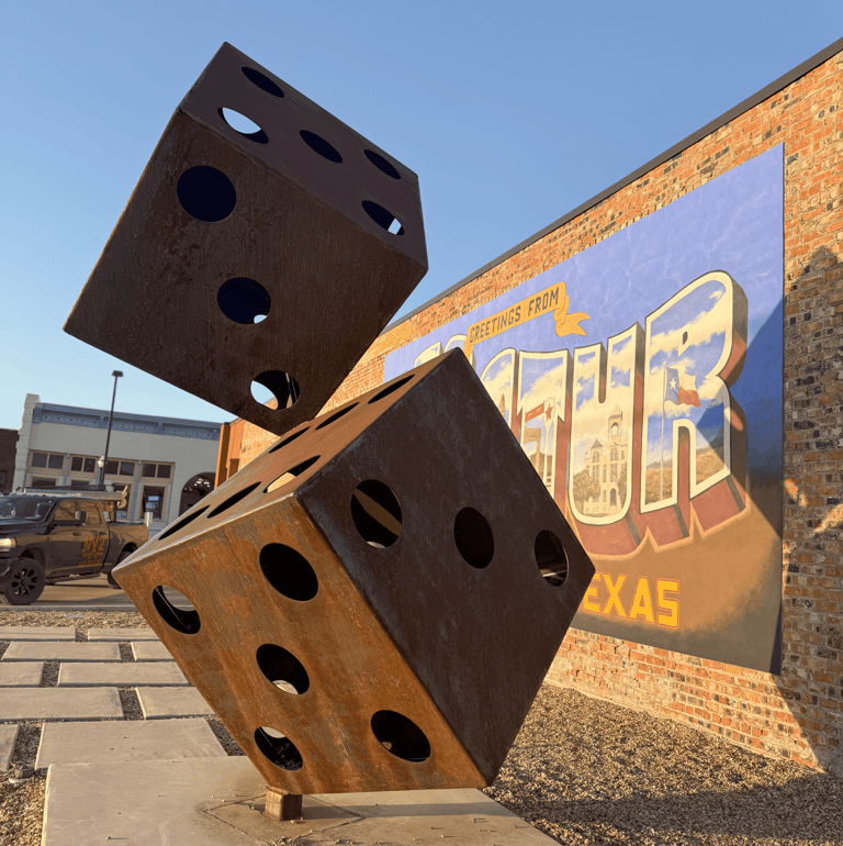 Metal rusted dice statue Decatur Texas mural behind it 