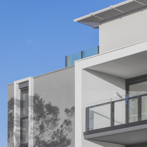 Modern apartment building with white and grey facade and glass balcony against a clear blue sky.