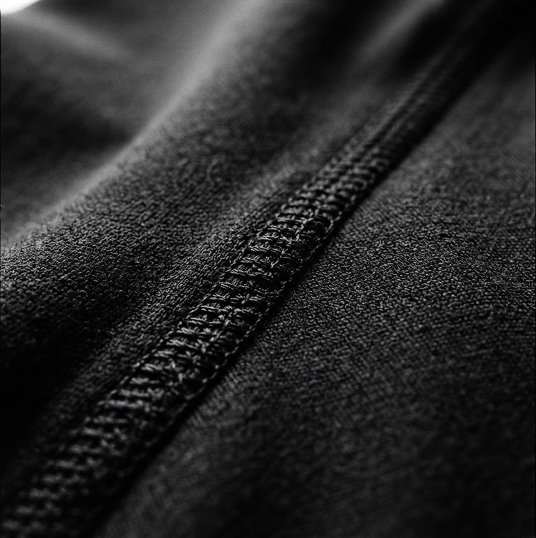 Close-up of technical stitching on raw black athletic fabric, dramatic studio lighting, stark monochrome tones, sharp focus, 35mm film