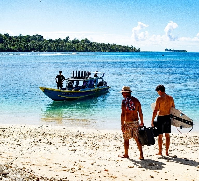 two men walking on the beach with a boat in the background