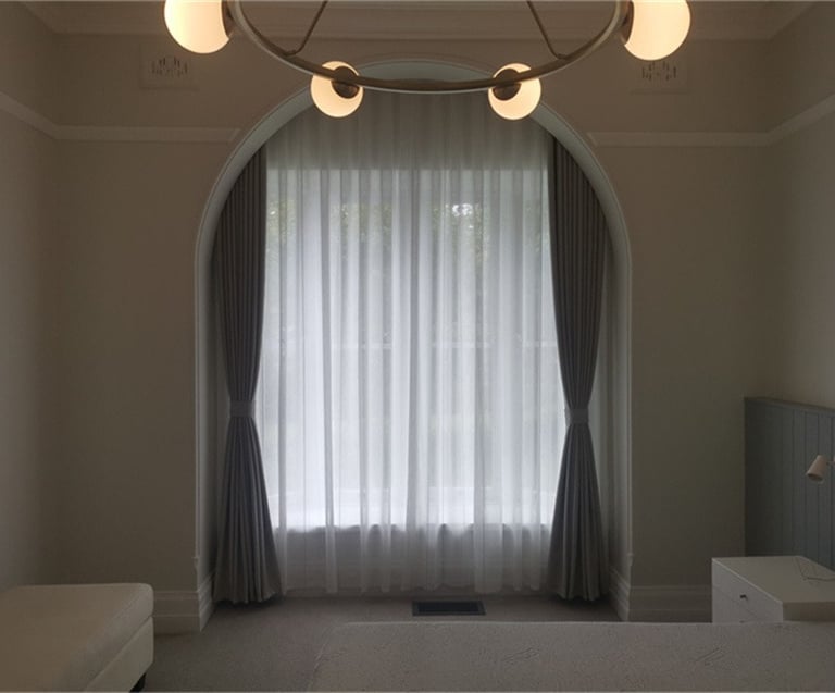 Elegant bedroom featuring a large arched window with white sheer curtains and blackout drapery.