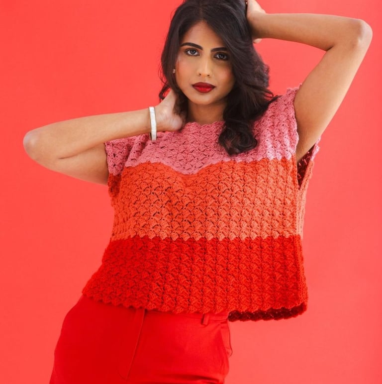 Woman wearing a handmade pink and red crochet shell stitch top against a bright red background.