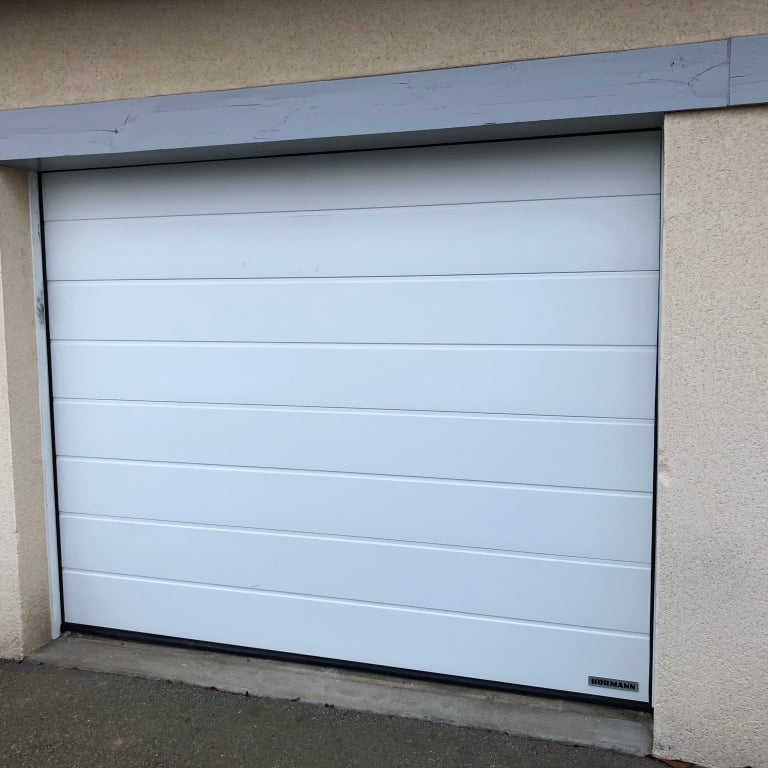 Porte de garage sectionnelle motorisée blanche à rainures horizontales installée en rénovation.