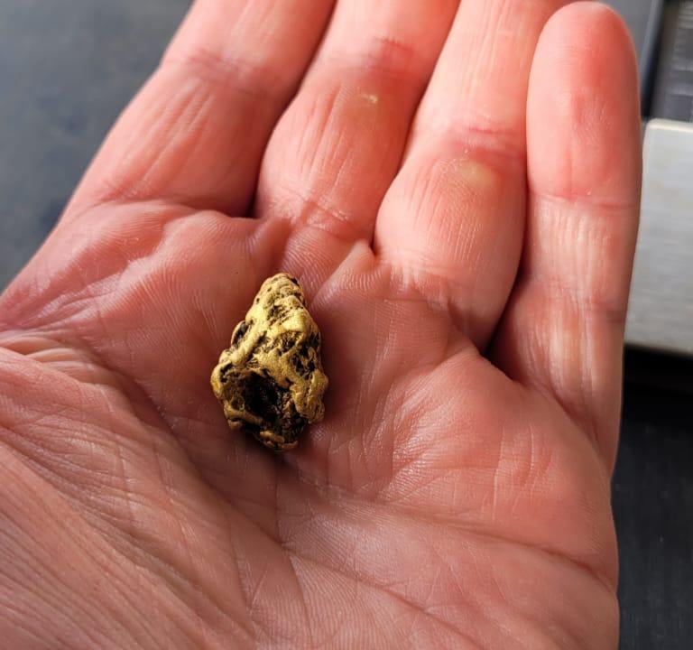 A hand holding a large gold nugget