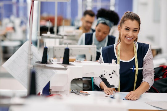 Smiling female seamstress working at an industrial sewing machine in a garment factory.