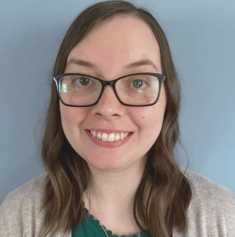 kristin gunner, doula, with glasses, smiling in front of a blue background