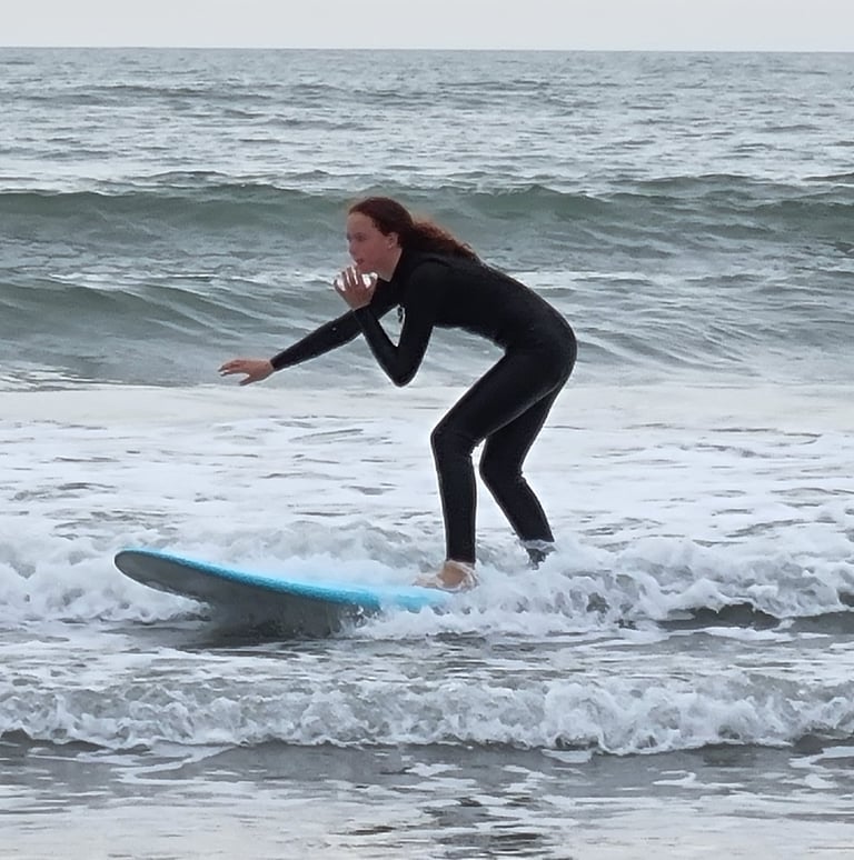 A female surfer riding a baby blue surfboard and a small broken wave.