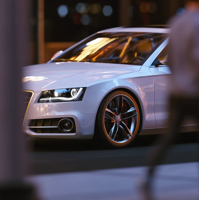 A white luxury sedan parked on a city street at night with glowing headlights and blurred city lights.