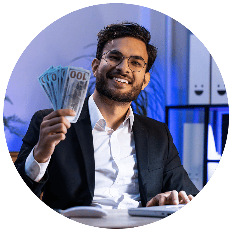Smiling businessman in a suit holding a fan of hundred dollar bills at a desk.