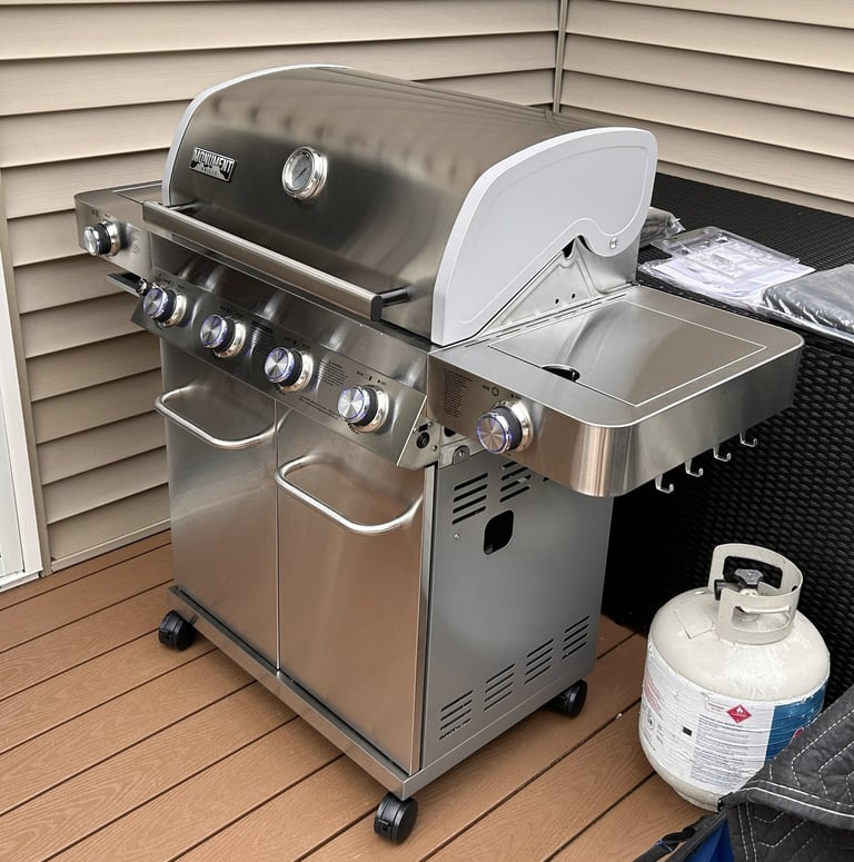 Left side view of stainless steel propane grill showing side burner and hooks