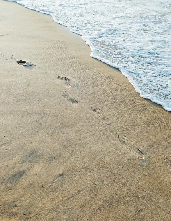 a beach shore with footprints imprinted into the sand going along the water's edge