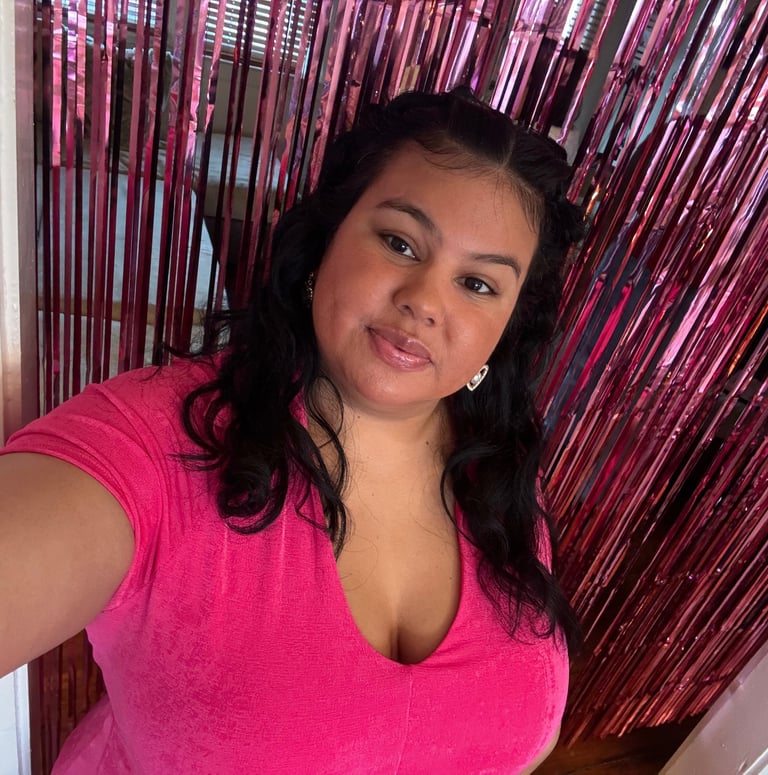 A smiling woman in a pink t-shirt poses in front of a shiny pink foil fringe backdrop.