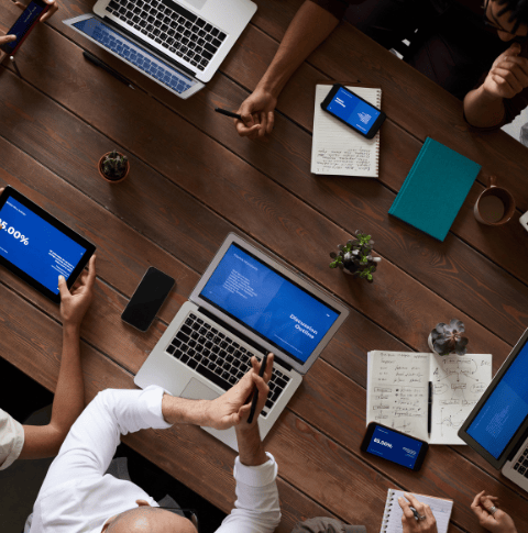 Seen from above - A team gathers at a large table with notebooks and laptops ready 