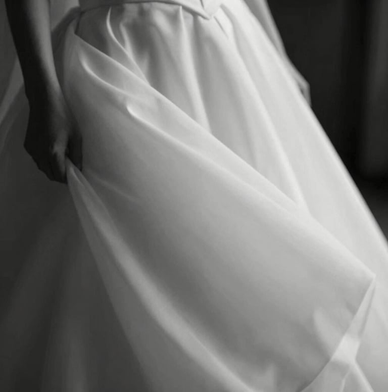An artistic black and white style photograph using dark charcoal and soft off-white tones. It depicts a candid, blurry movement of a wedding dress fabric, evoking a sense of calm and sophisticated movement. Professional and high-end.