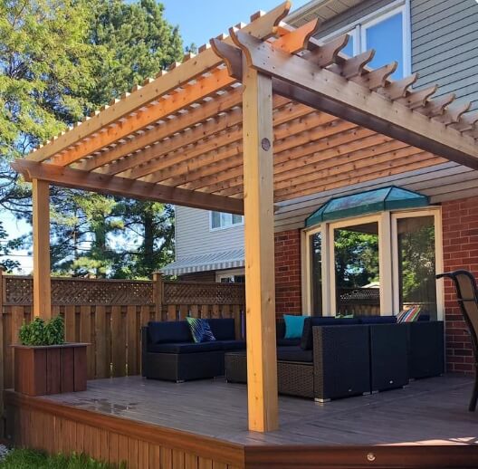 Wooden pergola built over a backyard deck with outdoor seating attached to a house.