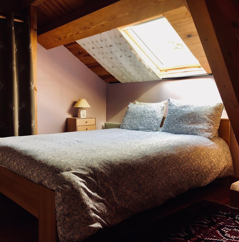 grand lit dans une chambre de la grange russell avec un velux, un rideauet une lampe de chevet