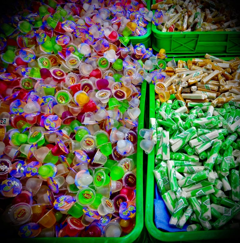 Assorted colorful mini fruit jelly cups and wrapped chewy candies in green plastic bins.