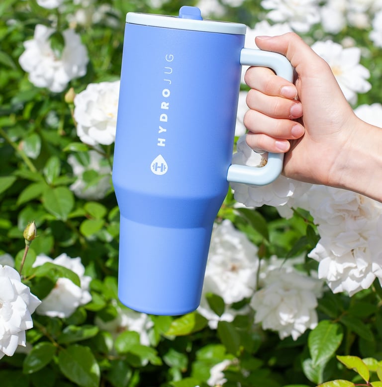 a person holding a blue coffee mug in front of a bush