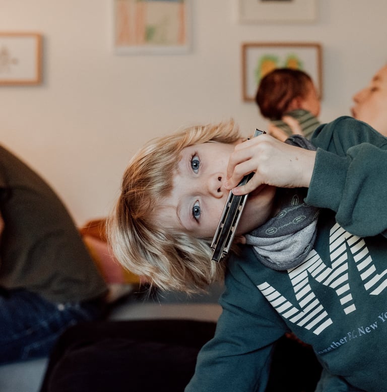 Ein junger blonder Junge spielt Mundharmonika, während sich seine Familie in einem Wohnzimmer