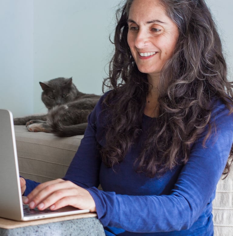 Porträt von Juliette Maggu am Laptop mit einer Katze im Hintergrund