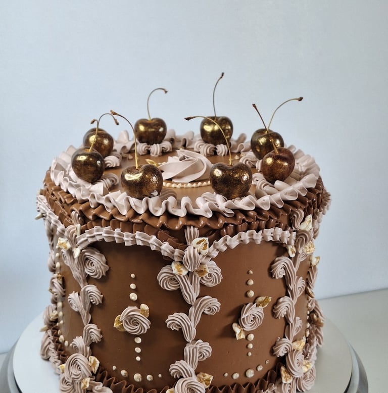 Elegant chocolate vintage cake with ornate piping and gold-dusted cherries on top.