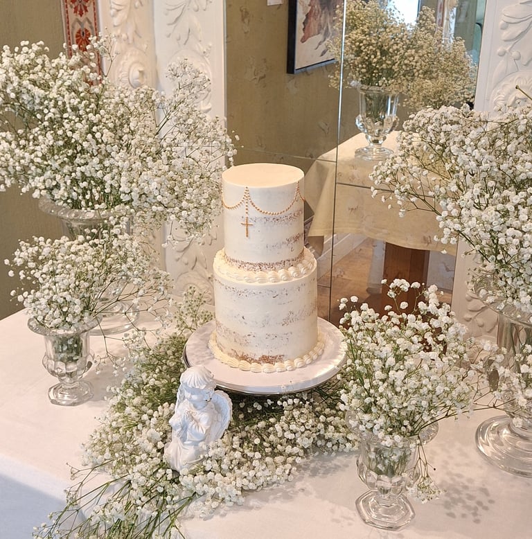Elegant two-tier white baptism cake with gold cross and baby's breath floral arrangements.