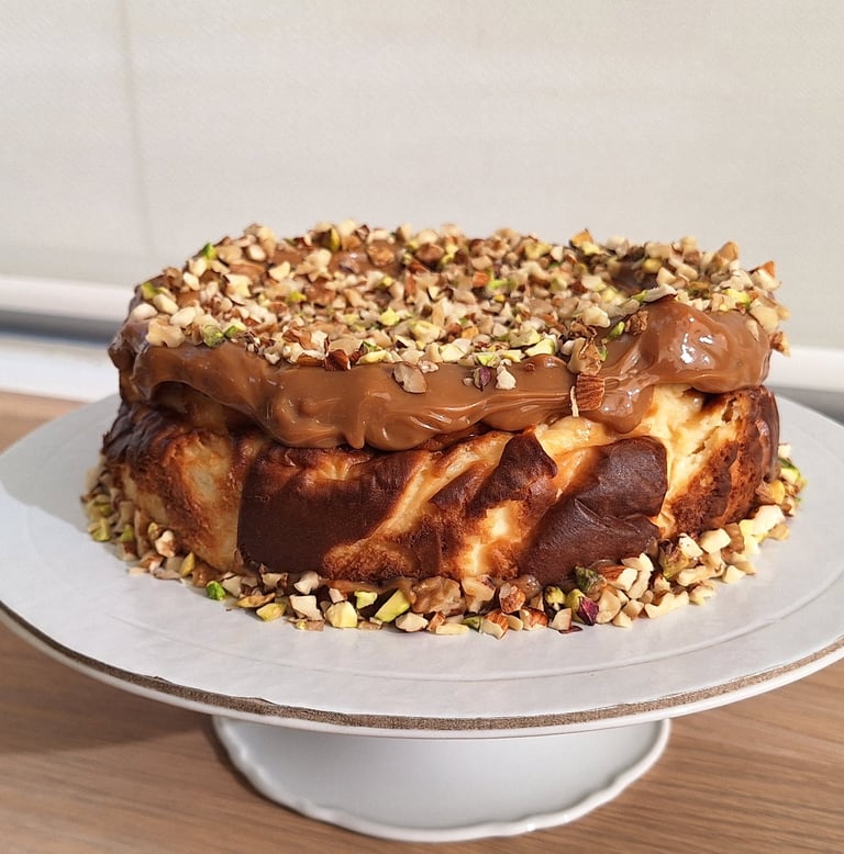San Sebastian burnt cheesecake topped with creamy caramel and crushed pistachio nuts on a white cake stand.