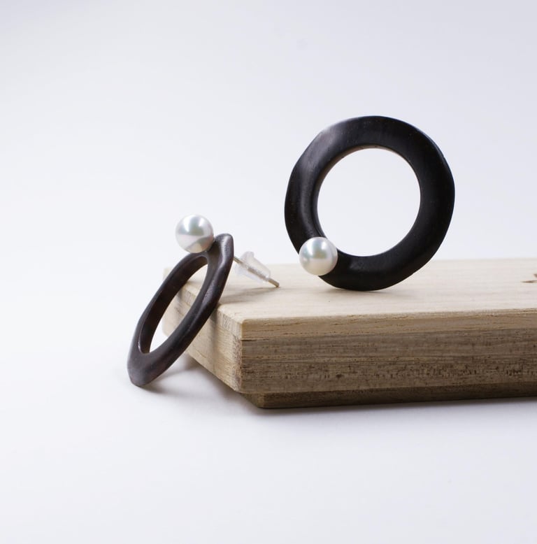 Handmade black ebony wood hoop earrings with white pearls displayed on a wooden block.
