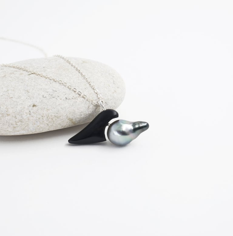 Handmade silver necklace featuring a black onyx gemstone and a grey baroque pearl on a white stone.