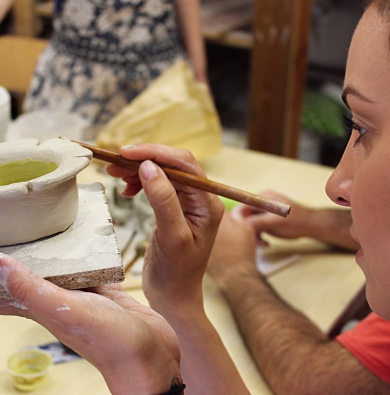 a woman is painting a clay potted with a brush