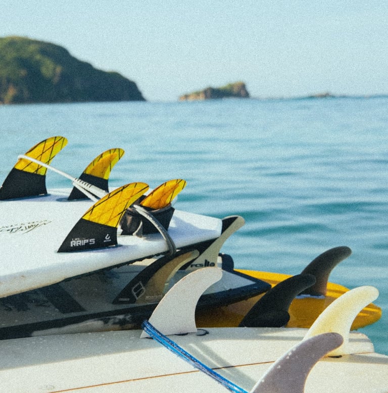 A stack of colorful surfboards with fins attached resting on a boat in the ocean.