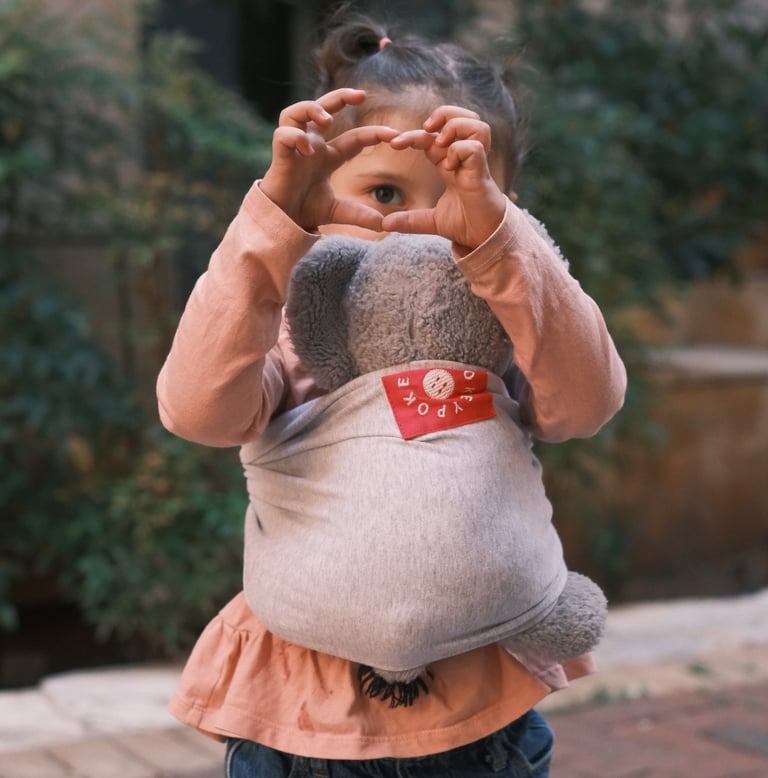 a little girl holding a stuffed animal in a babywrap carrier