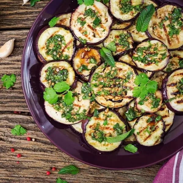 Grilled eggplant slices garnished with fresh herbs on a purple plate