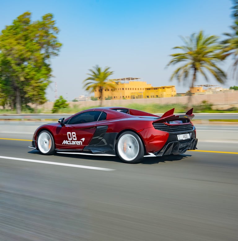 A red McLaren 650S Spider luxury supercar driving fast on a highway with palm trees.