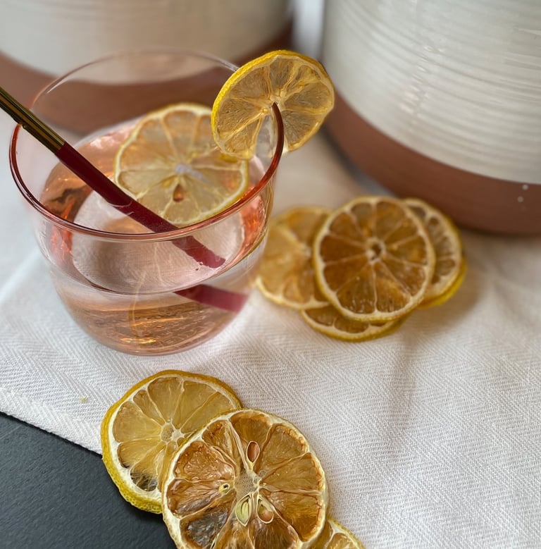 dehydrated lemons displayed in and around pink water glass with metal straw in front of plants