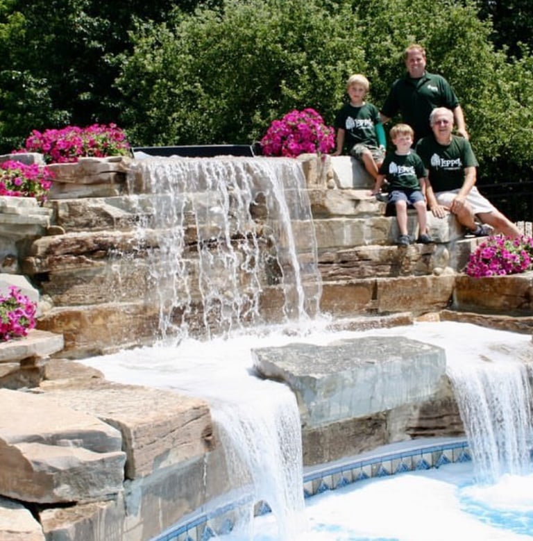 Leppek Landscape designed waterfall spilling into pool, surrounding landscaped patio.