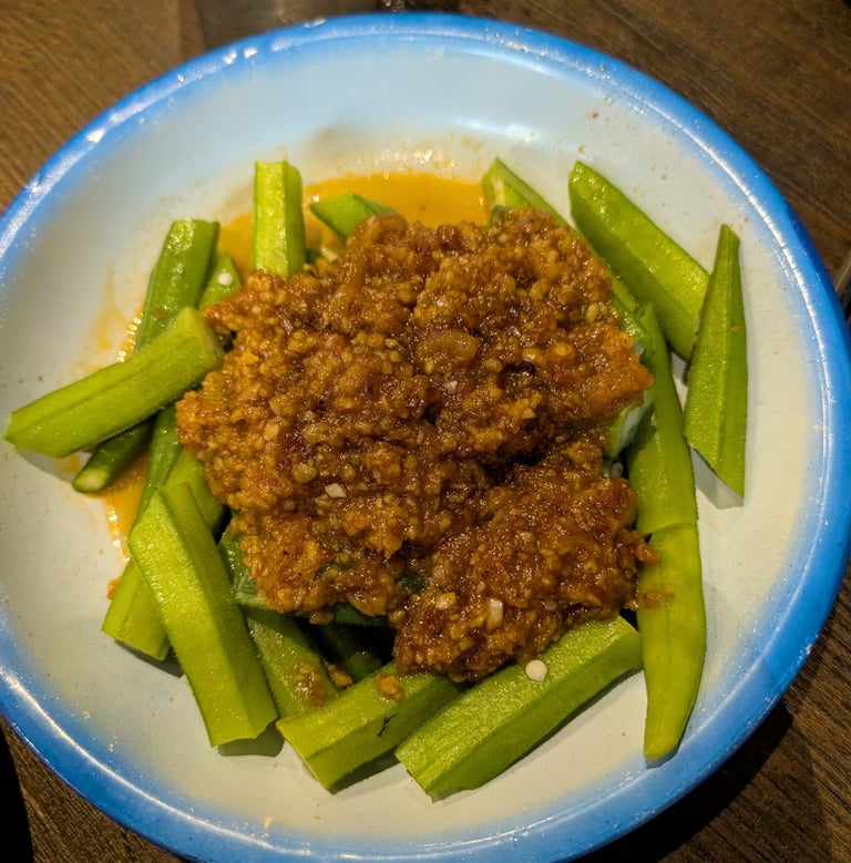Steamed okra pieces topped with savory minced meat sauce in a blue-rimmed white bowl.