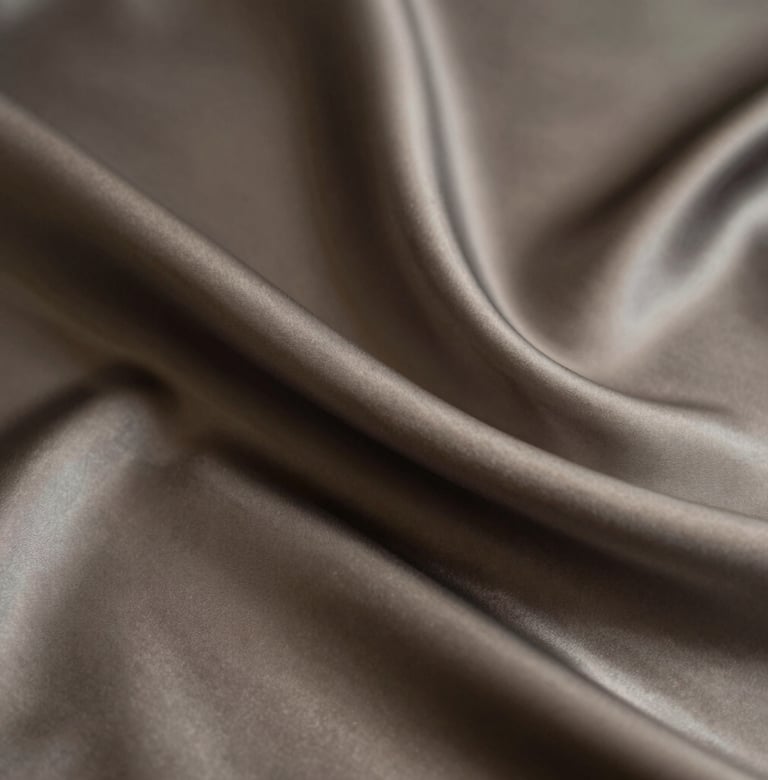A minimalist composition of fine silk fabric draping in the dark, with soft light catching the edges in beige and charcoal tones, reflecting luxury and distinction.