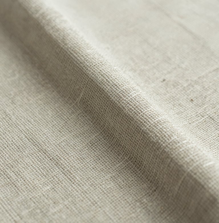 A macro photograph focused on the texture of a hand-woven fabric. The colors are muted sage and ivory, showing the delicate interplay of fibers and the organic imperfections typical of high-end, artisan textile production.