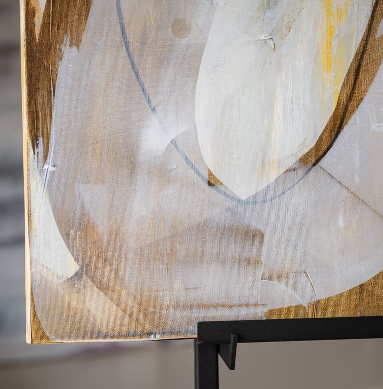 Abstract painting with textured brushstrokes of white, gold, and grey on a canvas.