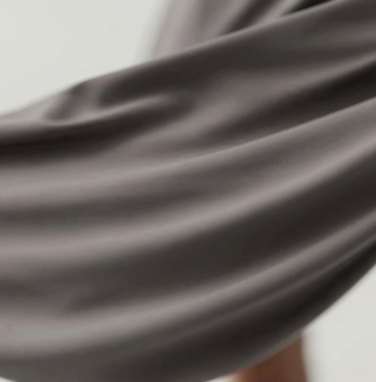 Abstract detail shot showing movement and motion blur of fabric. The colors are muted #4A616F and #1A1A1A, suggesting a high-speed cinematic capture with professional lighting.